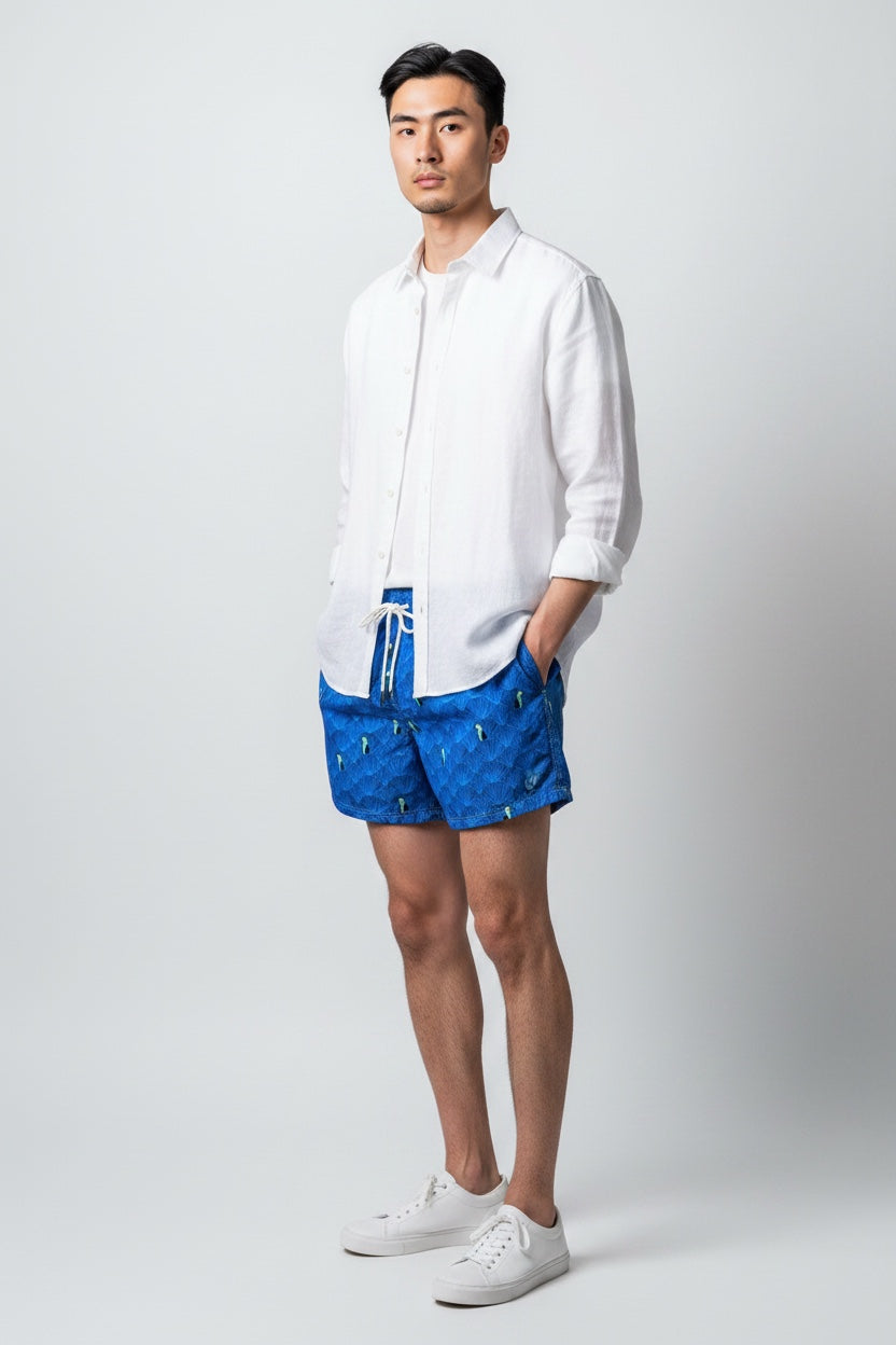 Model wearing 98 Coast men's blue toucan print swim shorts styled with a white shirt, side view
