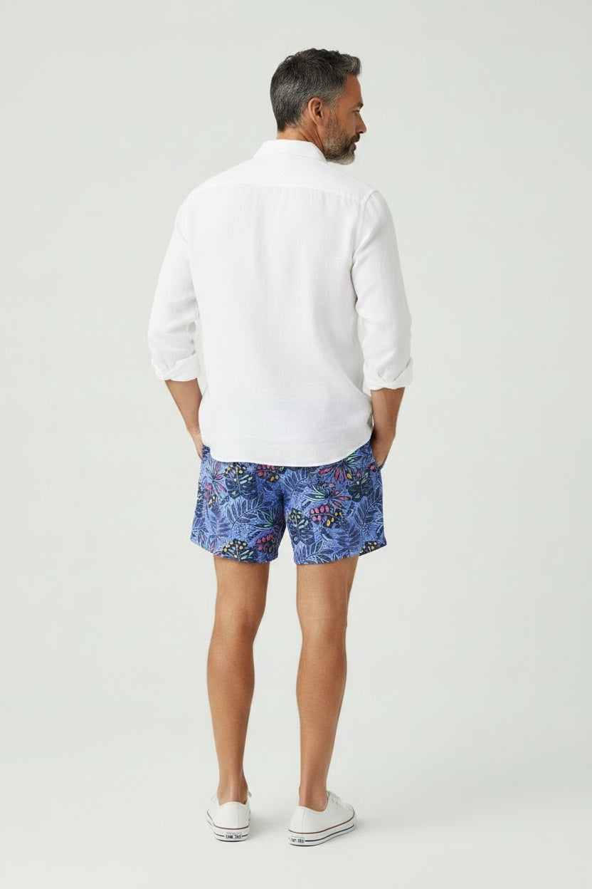 98 Coast Ave men's swim shorts in deep blue with a multicolored tropical leaf print and white shirt, model, back view