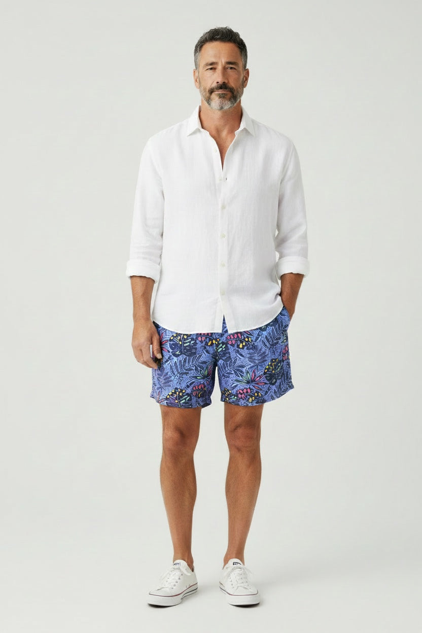 98 Coast Ave men's swim shorts in deep blue with a multicolored tropical leaf print, white shirt, model, front view