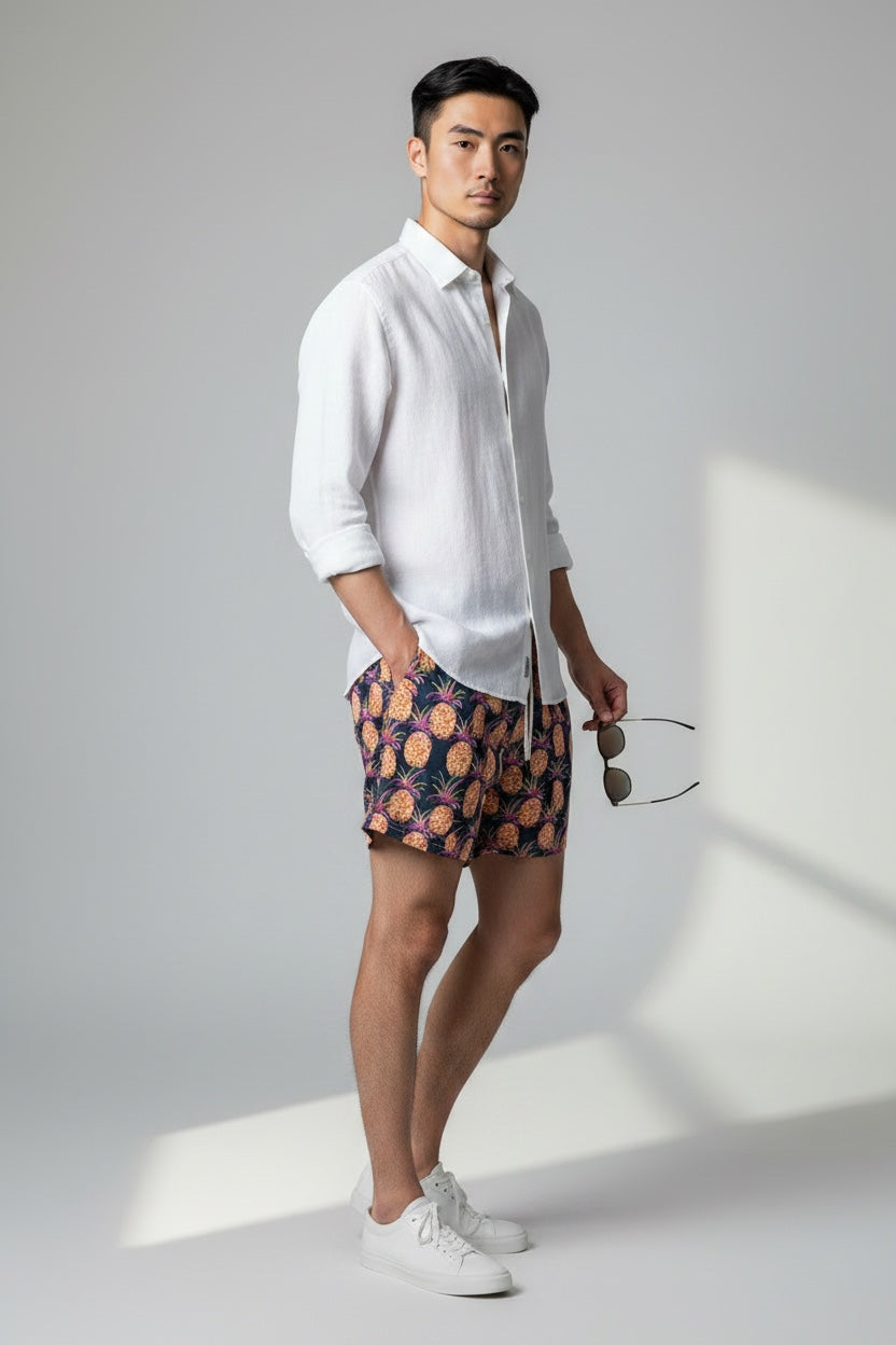 98 Coast Av. men's navy blue swim shorts with tropical pineapple print, elastic waistband and white drawstring, model wearing white shirt, side view
