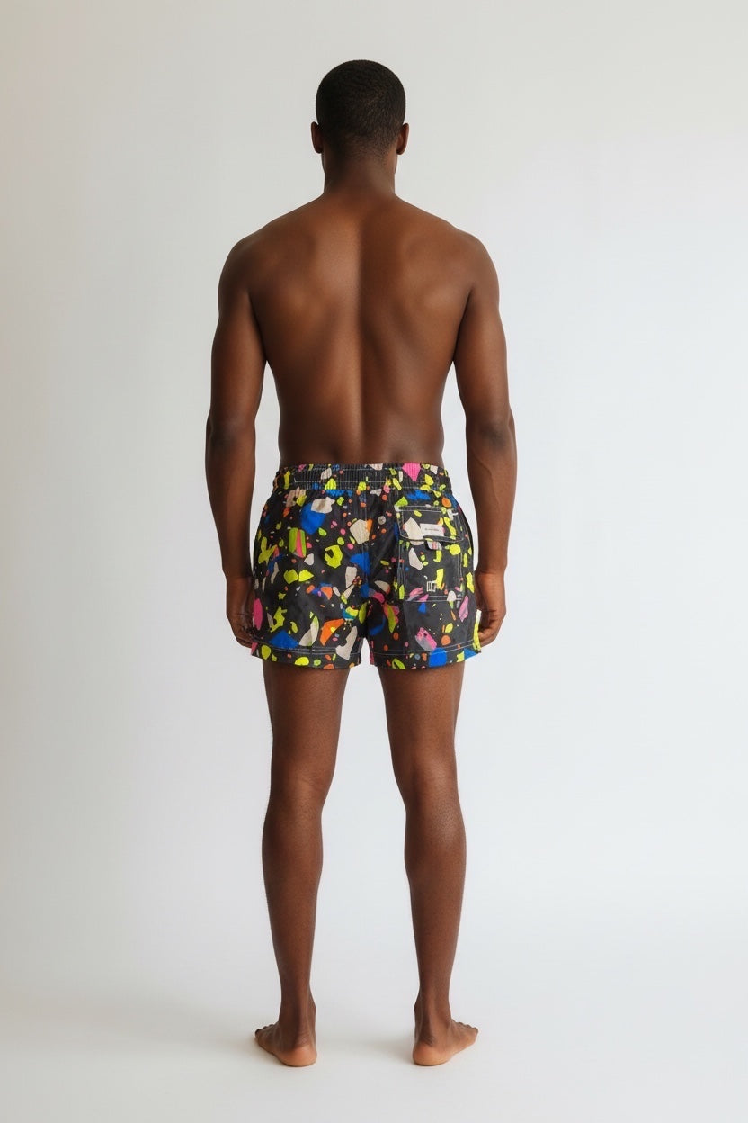 98 Coast men's black swim shorts with vibrant multicolor paint splatter print, elastic waistband and drawstring, back pocket detail, model, back view