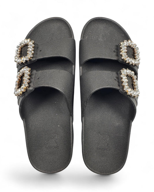 Cacatoes matte black slide sandals with dual straps and sparkling rhinestone encrusted buckles top view
