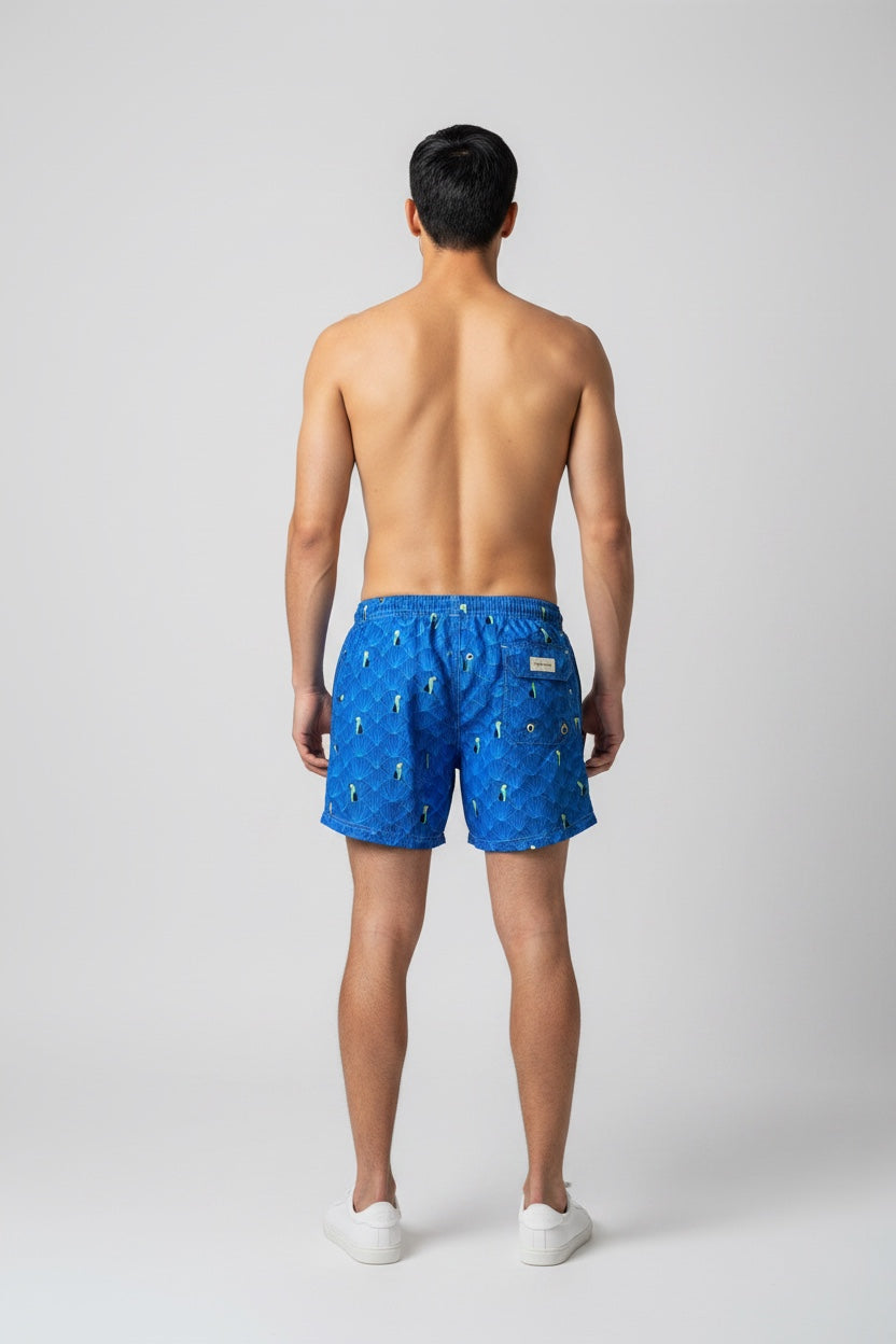 Model wearing 98 Coast men's blue toucan print swim shorts, elastic waist band and back pocket  detail. styled with a white shirt, model, back view