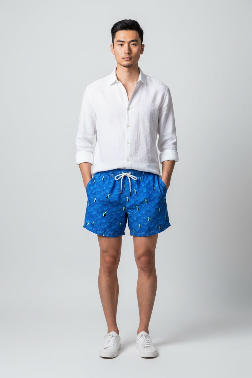 Model wearing 98 Coast men's blue toucan print swim shorts styled with a white shirt